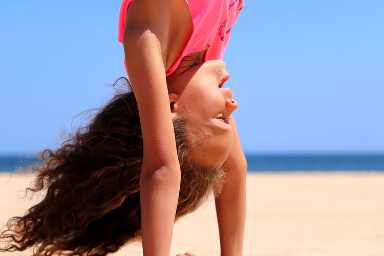 Girl doing handstand at beach against clear sky
