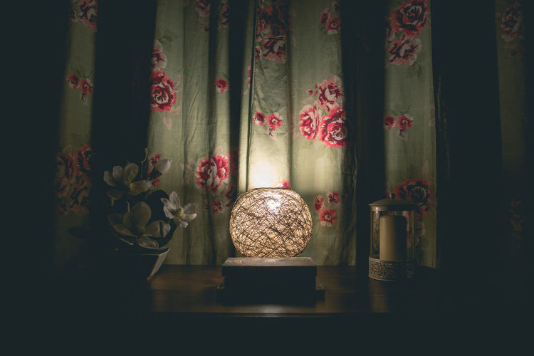 Illuminated lamp on table against curtain in darkroom