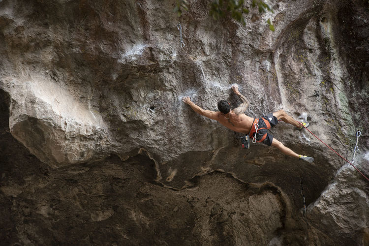 One tattooed man with no shirt stretches while rock climbing in mexico