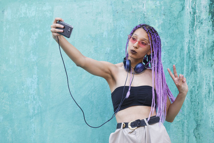 Woman with purple hair taking selfie while standing against wall