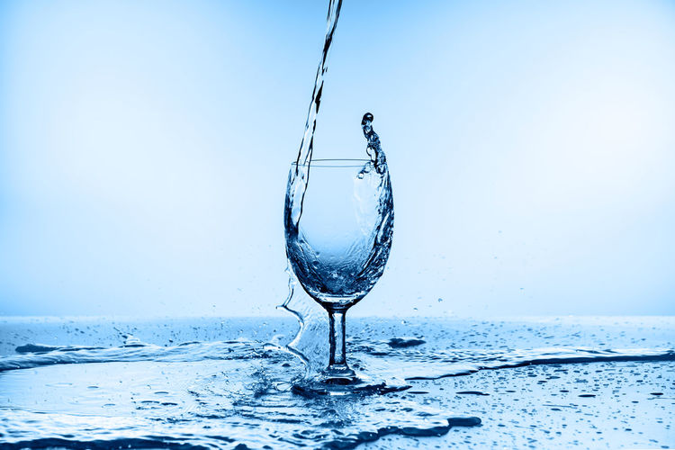Close-up of glass splashing water against blue background