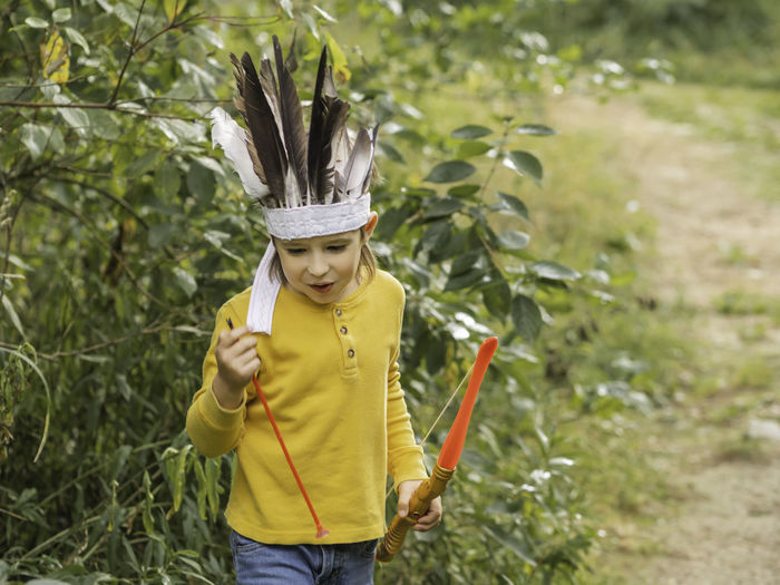 Boy plays american indian. kid has handmade headdress of feathers, bow with arrows. costume play. 