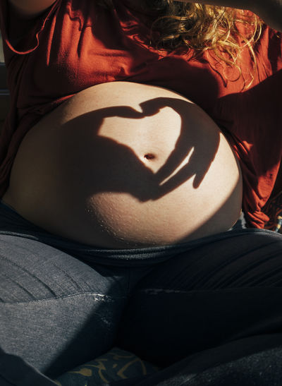 Shadow of hands making heart shape on pregnant belly