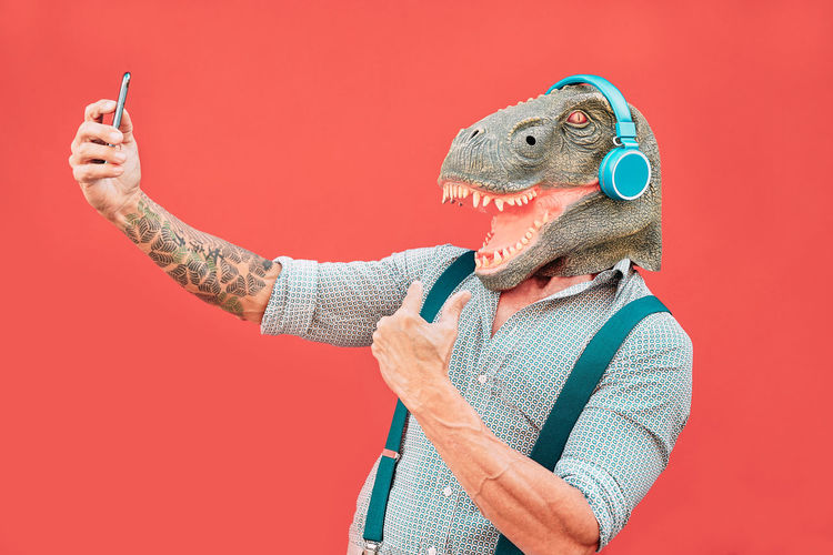 Man wearing dinosaur mask taking selfie against red background