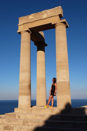Side view of woman leaning on column against blue sky