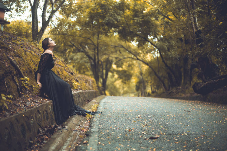 Woman sitting on road amidst trees