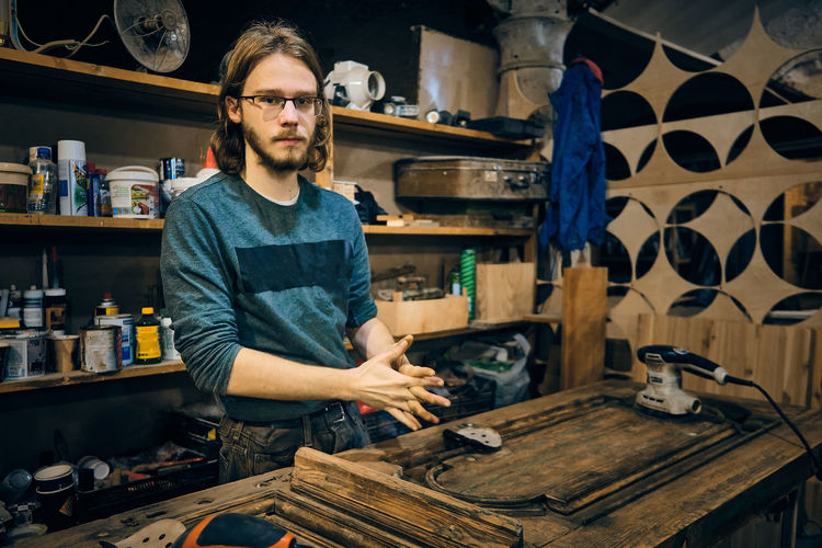 Portrait of young adult man at carpenter workshop. man works on vintage wooden door restoration