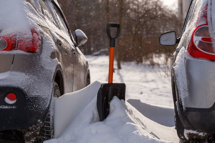 Small plastic shovel sticking out from a snowdrift between two cars in parking after a snow storm