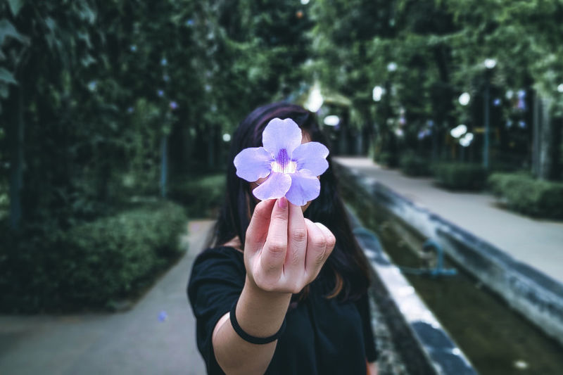 Woman holding purple flower against trees