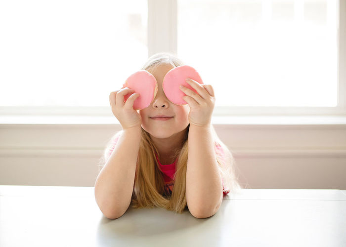 Cute blond girl holding pink frosted sugar cookies over eyes