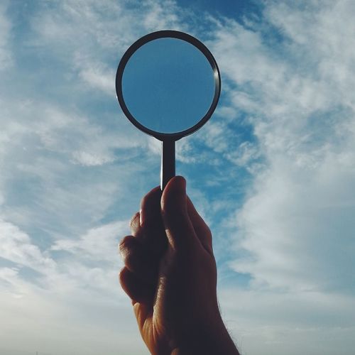 Cropped image of man holding magnifying glass against sky
