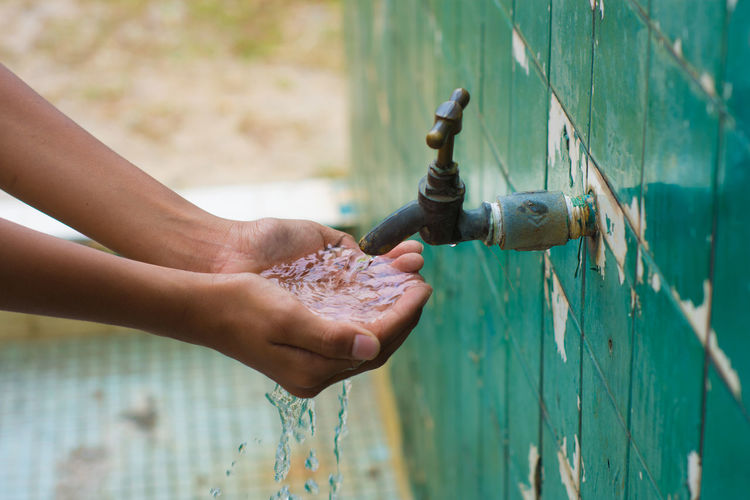 Cropped image of person washing hands in running water outdoors