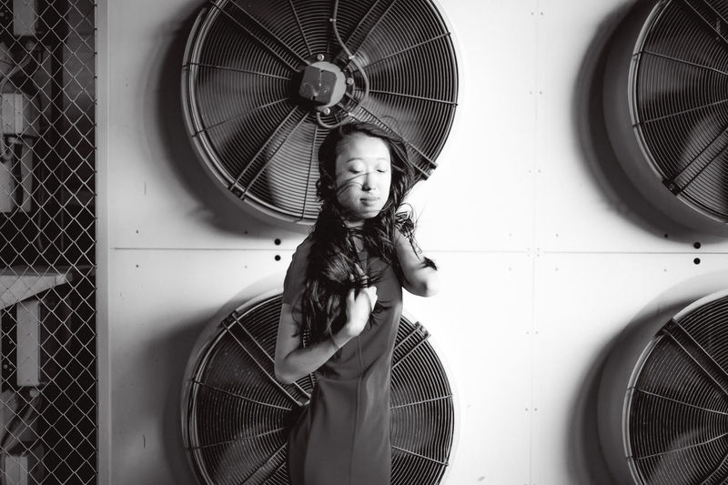 Young woman with tousled hair standing against exhaust fans