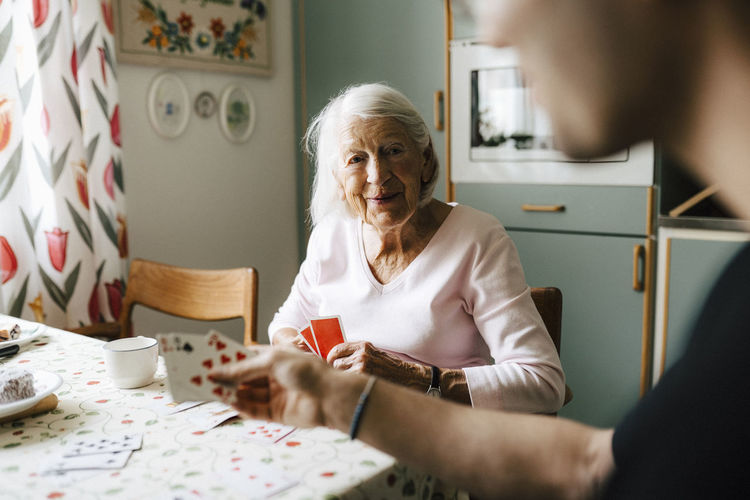 Elderly woman playing cards with male nurse at dining table
