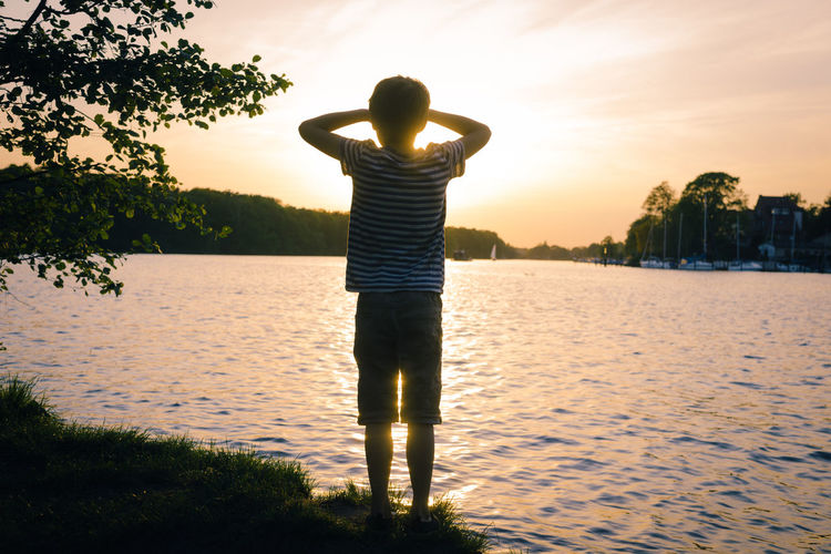 Rear view of man standing at lake during sunset