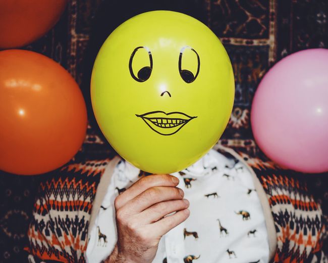 Close-up of man holding yellow smiley balloon