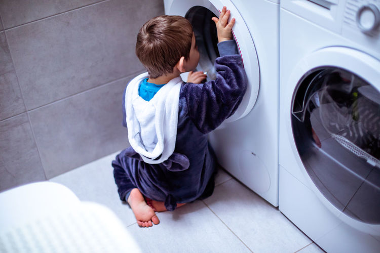 Rear view of boy peeking in washing machine