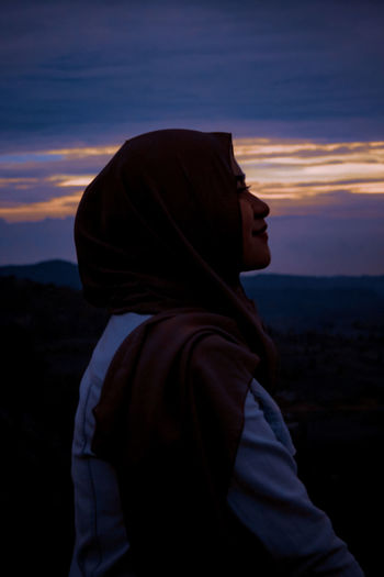 Side view of young woman looking at sunset