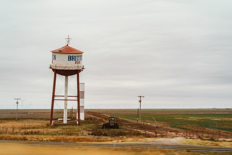 Water tower on field by building against sky