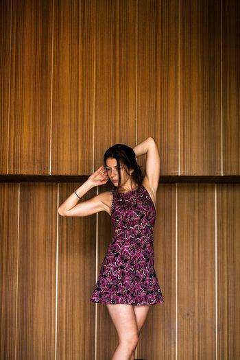 Young woman in magenta dress standing against wooden wall