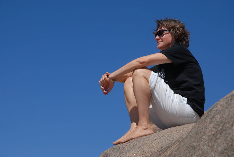 Low angle view of woman sitting on rock at magnetic island against clear sky