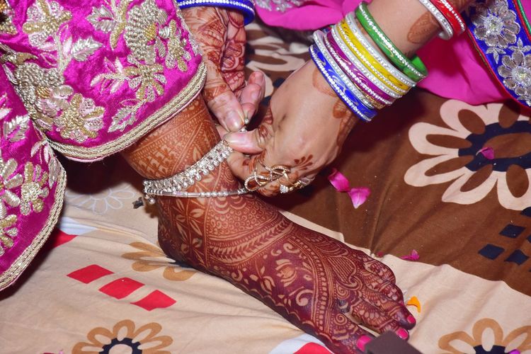Cropped hands of woman wearing anklet to bride in wedding ceremony