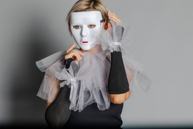 Woman in white theater mask and harlequin collar on gray background. fancy dress, masquerade clothes