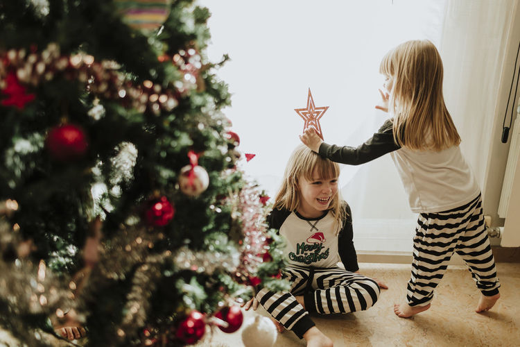 Sisters playing with christmas decoration against wall at home