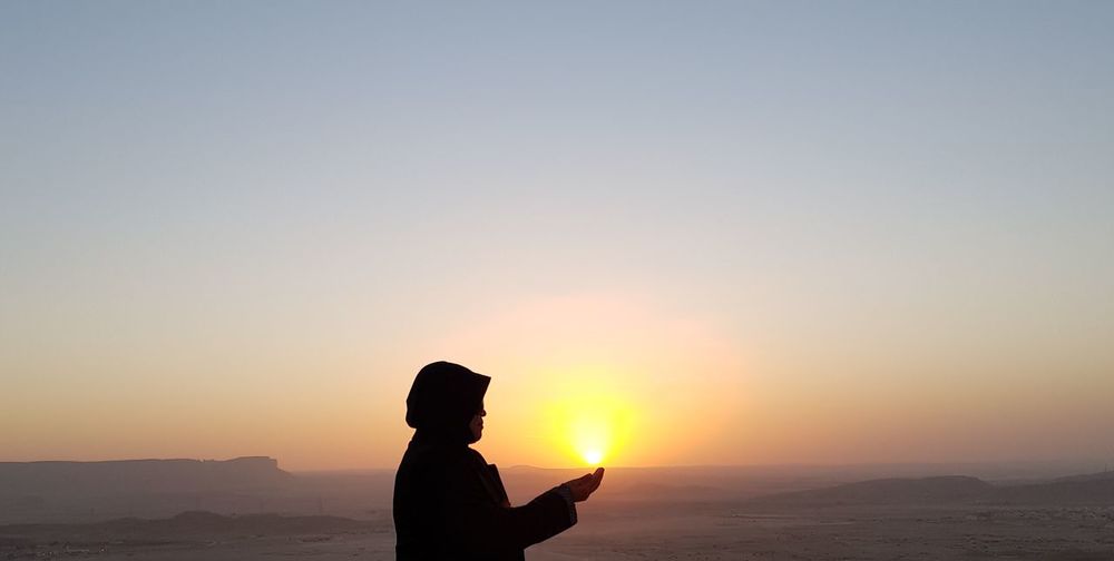 Optical illusion of person holding sun at sunset