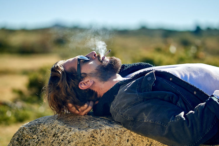 Portrait of young tattoed man lying on a rock smoking