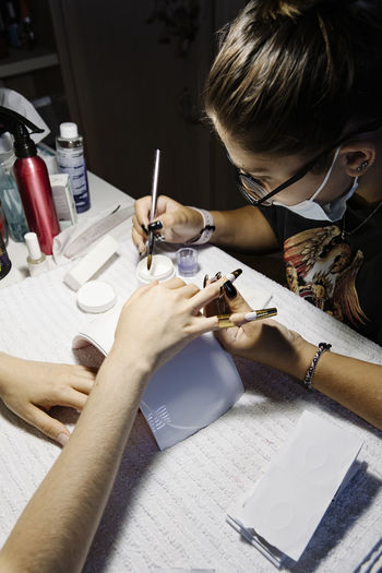 Woman in mask making french manicure to crop client during epidemic