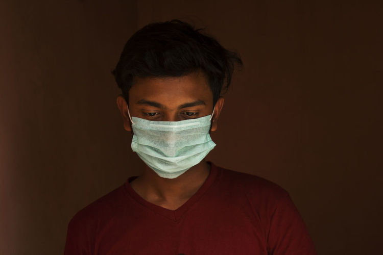 Close-up of young man wearing flu mask standing against black background
