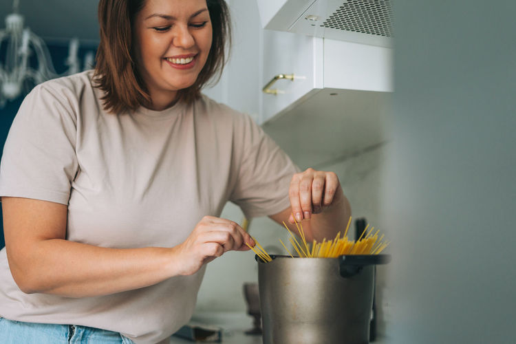 Beautiful brunette young woman plus size body positive cooking in kitchen at home