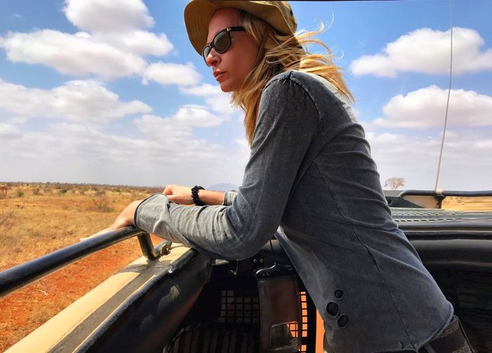 Side view of woman in off-road vehicle at tsavo east national park against sky