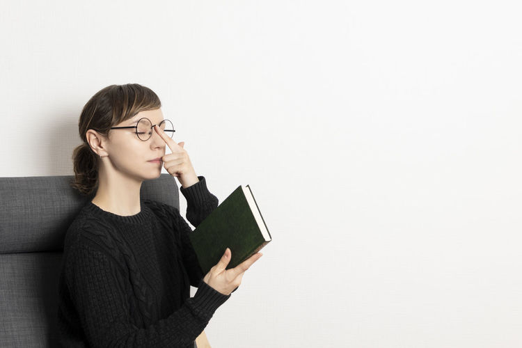 Portrait of young woman reading book against white background