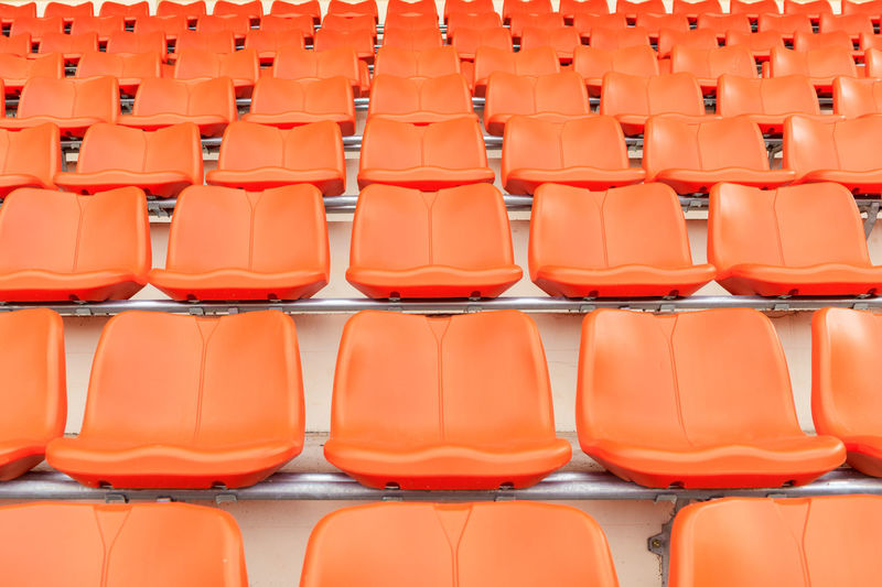 Rows of empty orange plastic grandstand seats at an indoor sport stadium. 