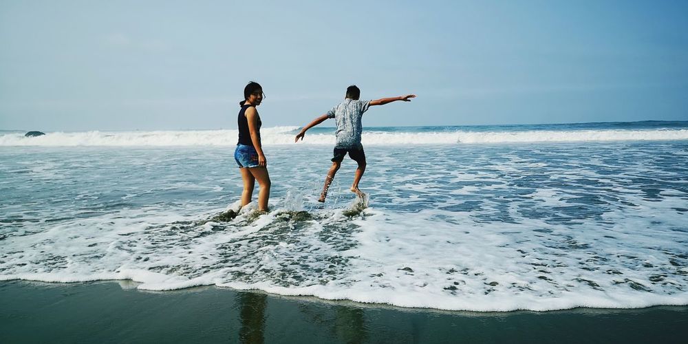 Portrait of smiling girl standing by brother jumping at beach