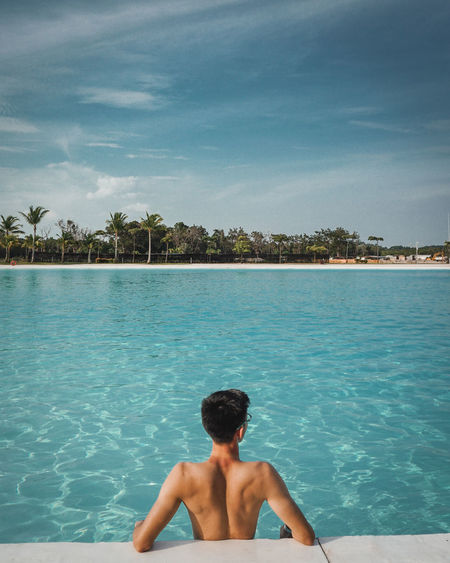 Rear view of shirtless man in infinity pool against sea