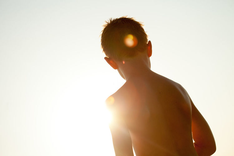 Silhouette shirtless boy against bright sky