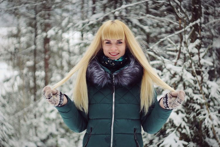 Portrait of smiling woman standing in forest during winter