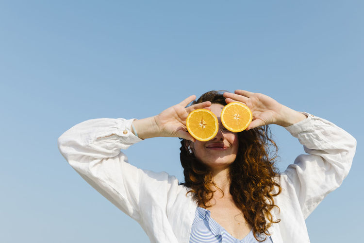 Smiling woman covering eyes with oranges on sunny day