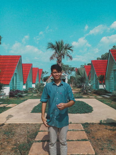 Young man standing against houses and sky during sunny day