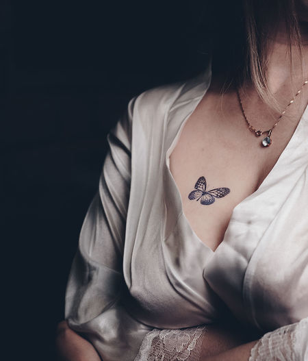 Midsection of woman with tattoo on breast against black background
