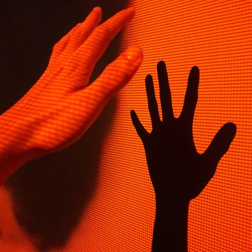 Cropped hand gesturing by wall with shadow in red illuminated room