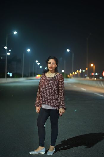 Portrait of smiling young woman standing on road at night