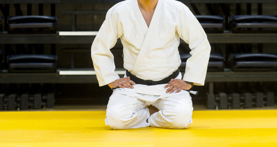 Low section of male judo sitting on floor against wall