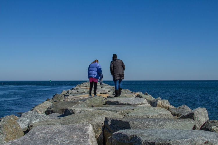 Family walking along rocky jetty at ocean in the wintertime