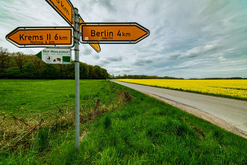 Road sign on field against sky
