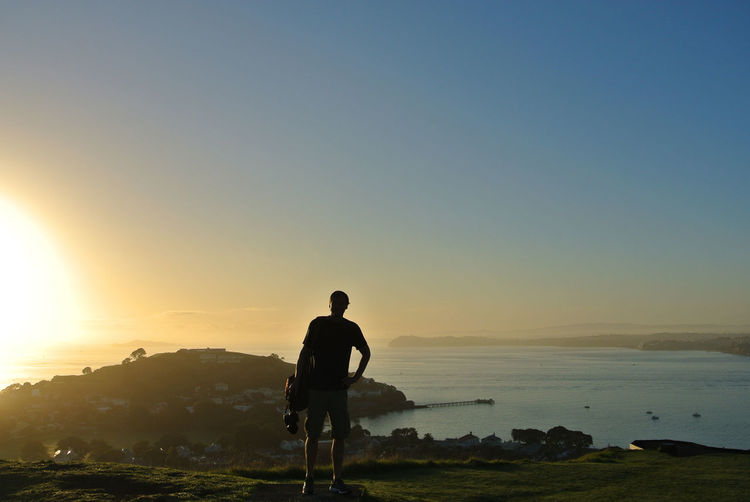 Full length of man standing against sea and clear sky during sunrise