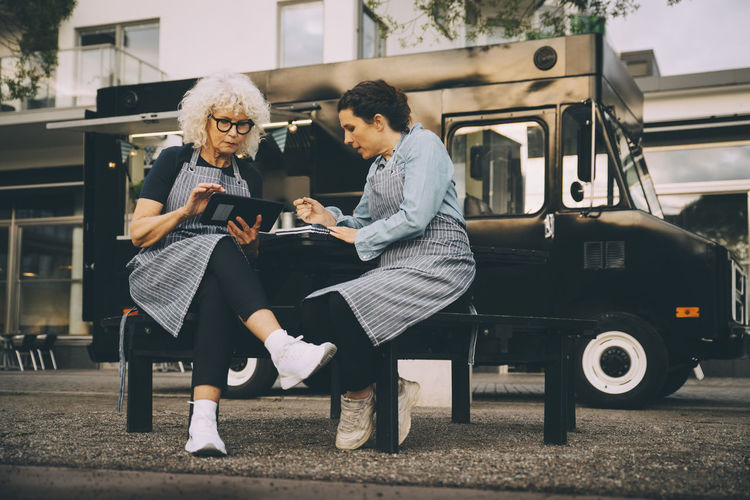 Senior female owner using digital tablet while sitting with partner against food truck